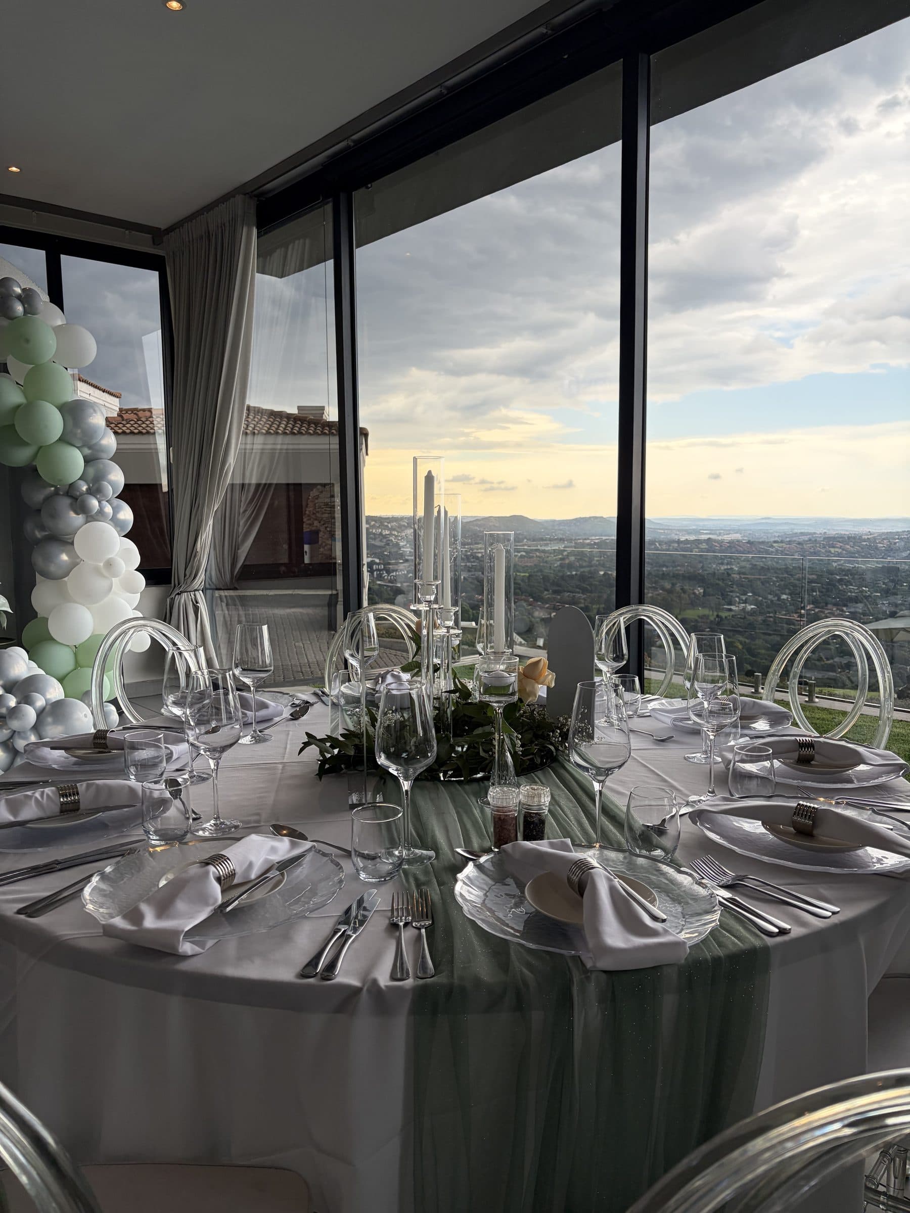 Fine-dining tablescape with sage runner and ghost chairs overlooking Johannesburg at golden hour