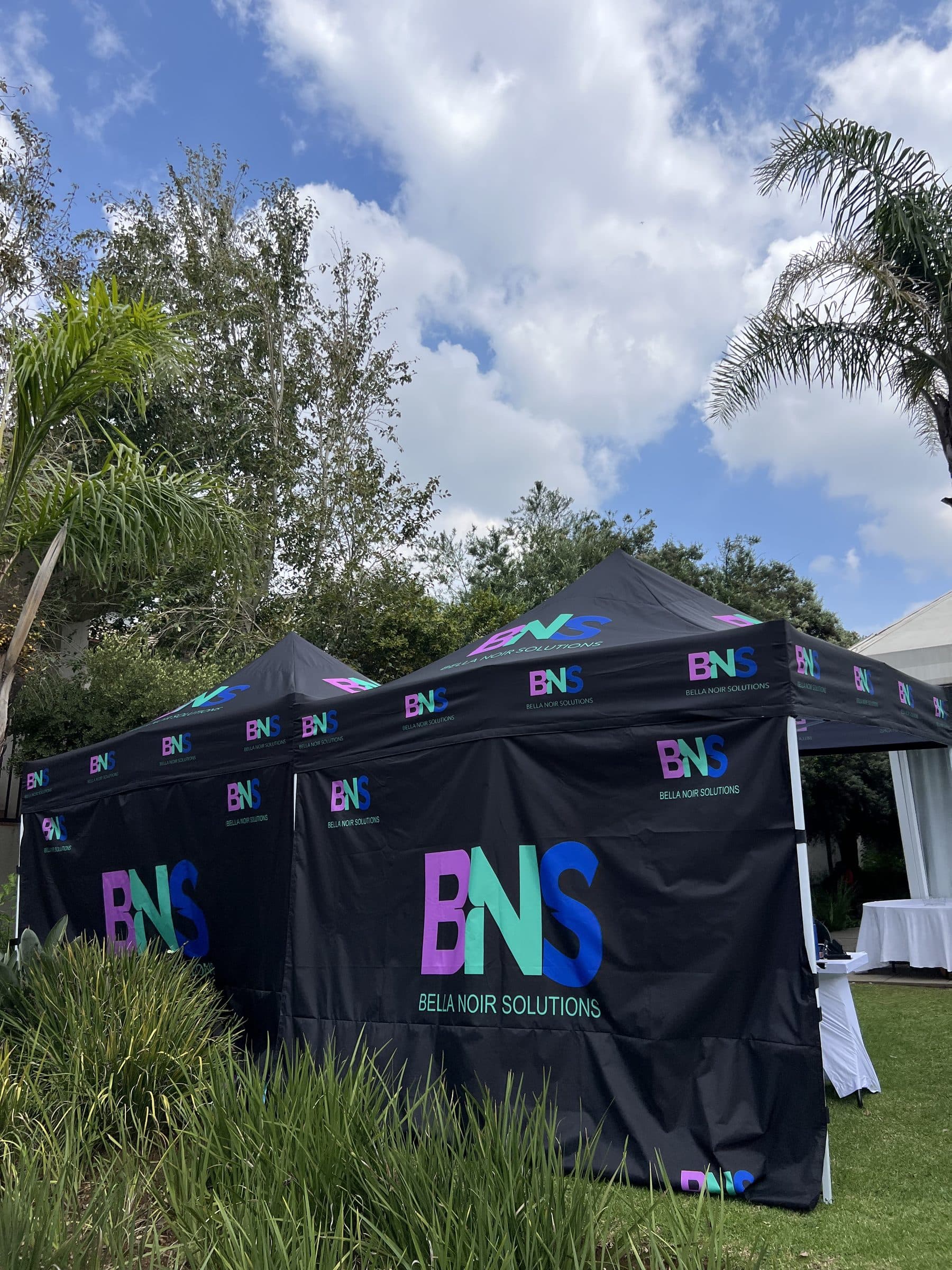 Black gazebo tents fully wrapped in Bella Noir branding on a garden lawn